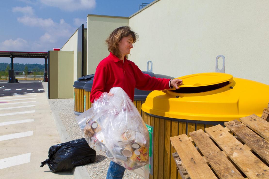 Femme jetant des déchets dans une poubelle de recyclage dans une station-service en France